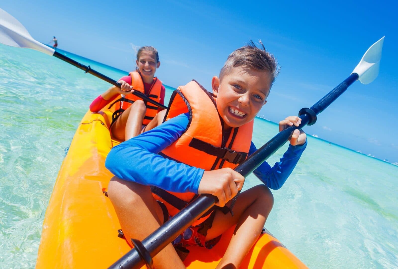 Kids kayaking in bright orange tandem kayak in shallow reef