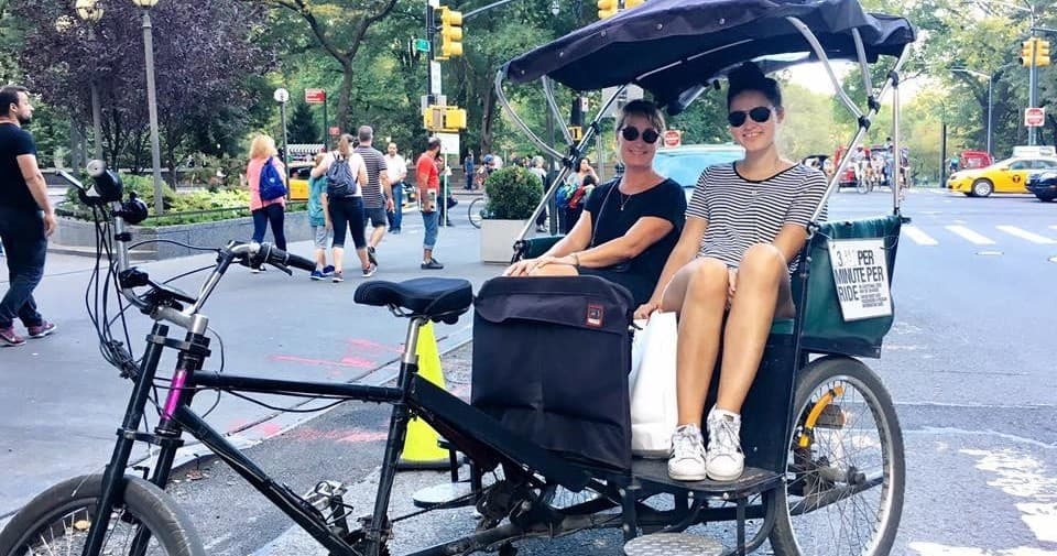 Two passengers riding a pedicab through park pathways, city sightseeing