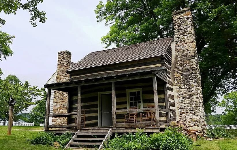 Historic log cabin porch with chimney in leafy rural setting