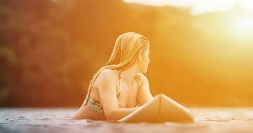 Surfer resting on board at sunset in warm coastal waters