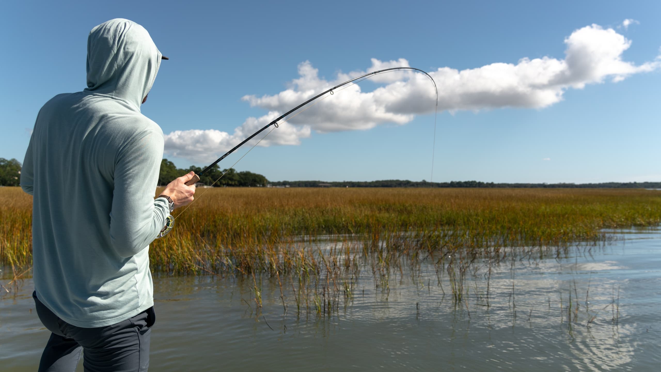 Angler casting in coastal marshes during sunny saltwater flats fishing