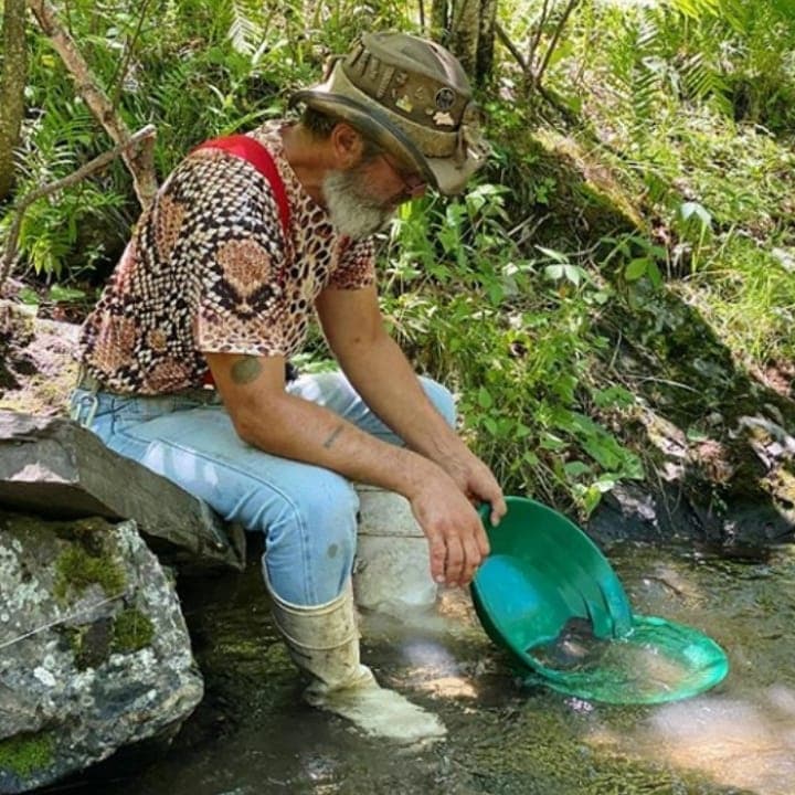 Man gold panning in shallow forest stream during prospecting trip