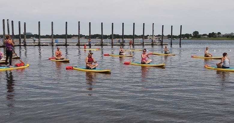 Group stand-up paddleboarding near wooden pier pilings on bay