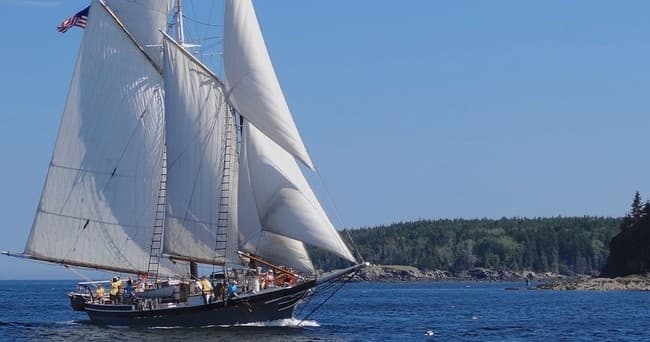 Sailing schooner under full sail on coastal ocean near rocky shore