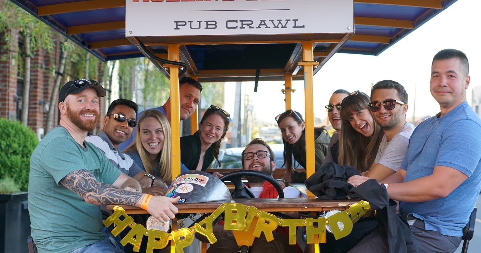 Friends on pub crawl pedal bike posing under canopy in town