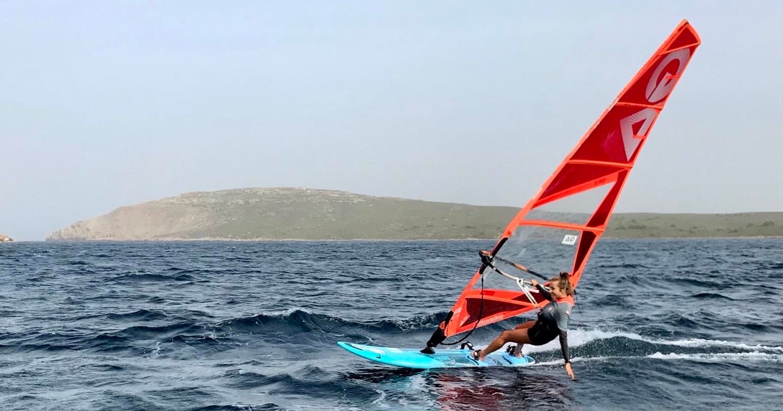 Windsurfer carving waves with red sail and distant island