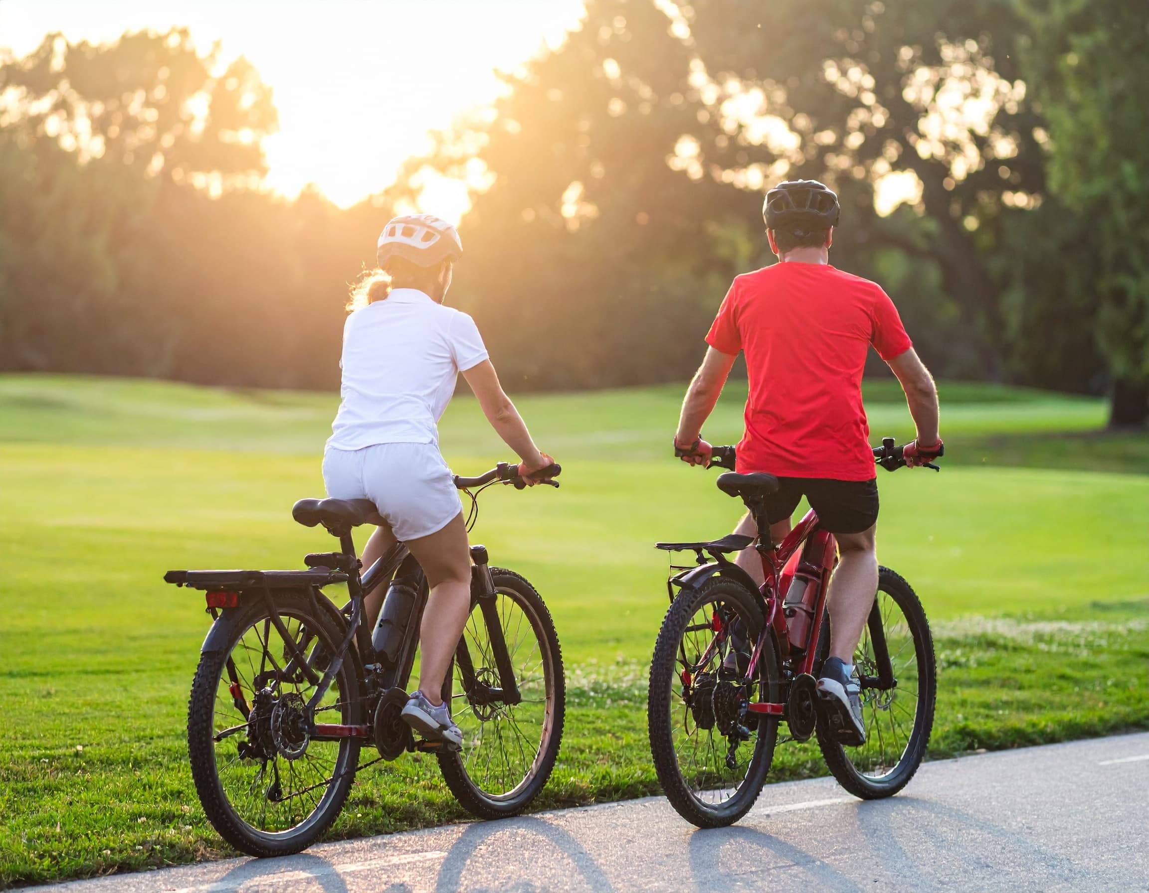 Couple cycling on park path at sunset across green fairway