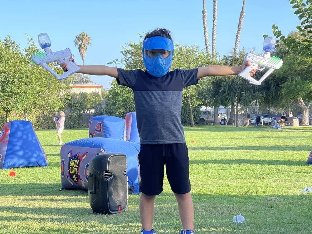 Child playing gel blaster in sunny public park field outdoors