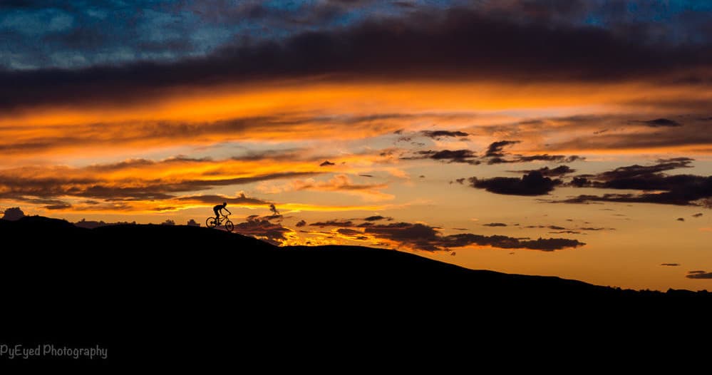 Cyclist silhouetted on ridge at dramatic mountain sunset