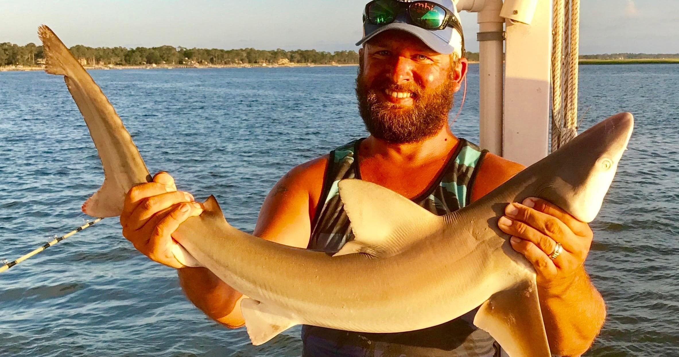 Fisherman holding a shark on deck during coastal shark trip