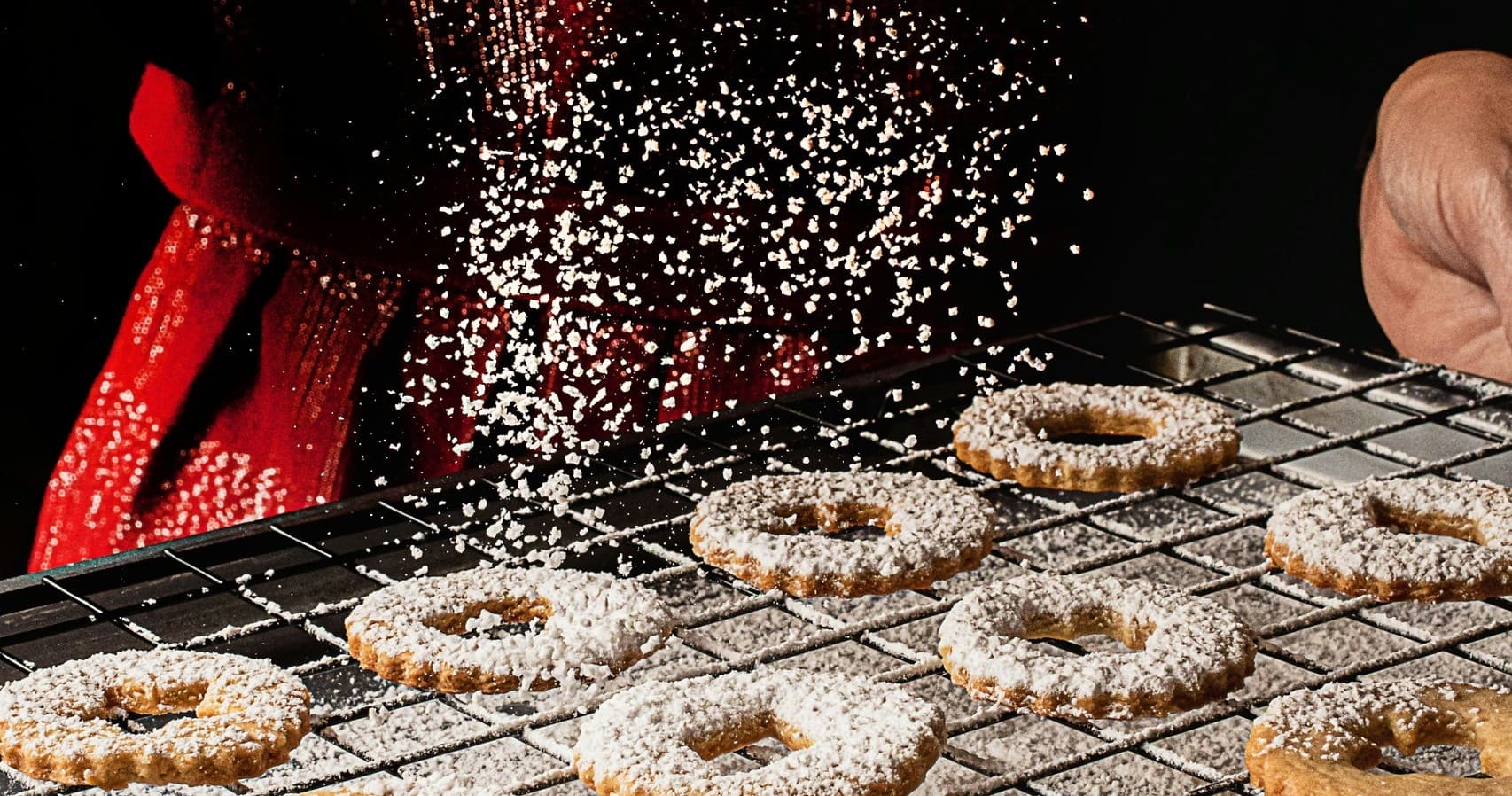 Chef dusting sugar on fresh doughnut rack, bakery prep station