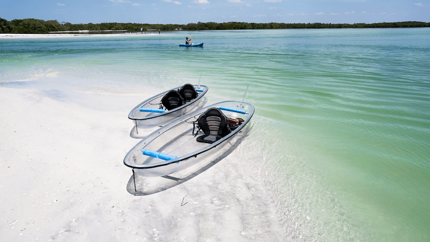 Clear kayaks resting on white sand by turquoise coastal lagoon