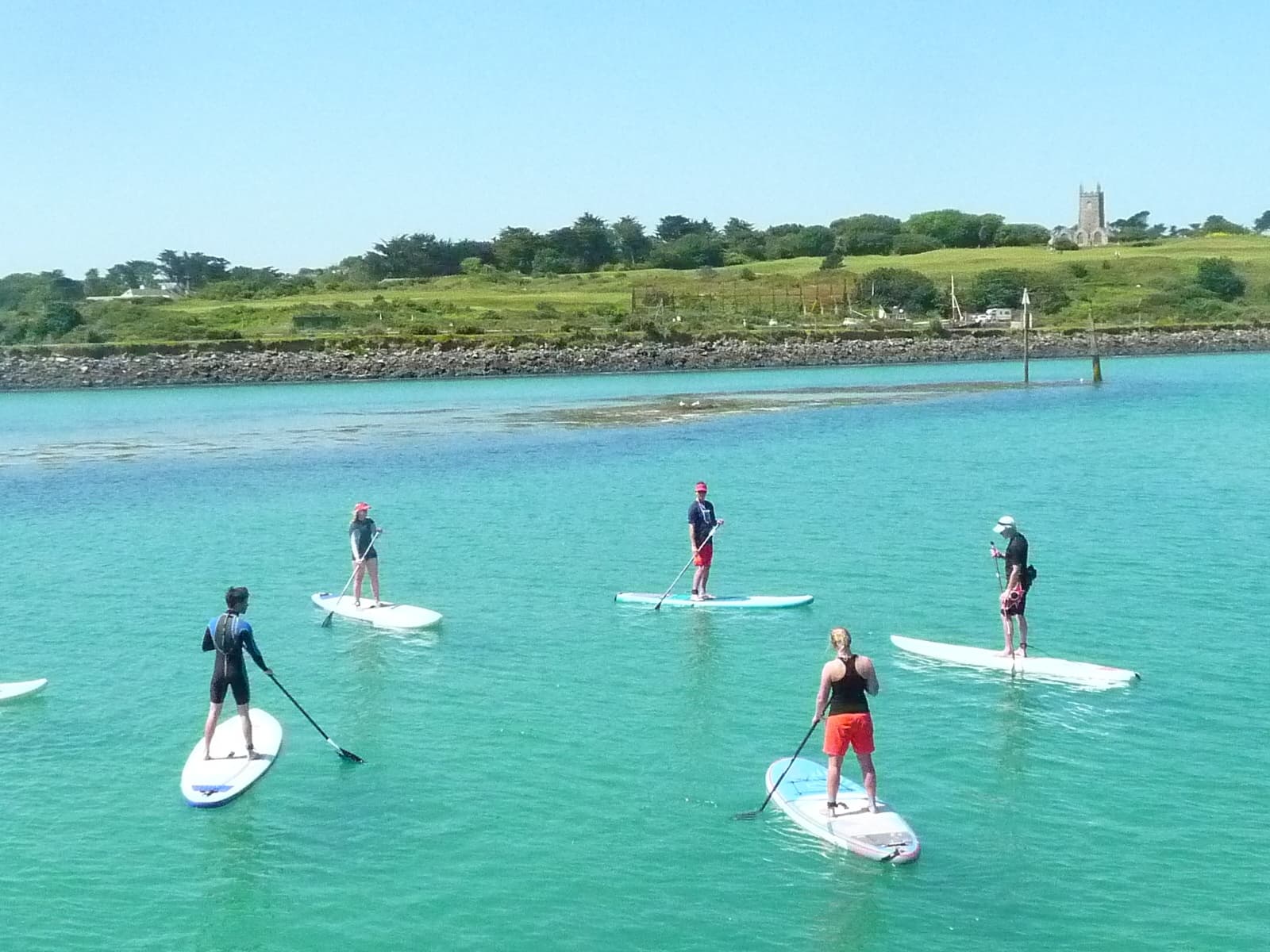 Stand-up paddleboarders cruising turquoise bay near grassy shoreline