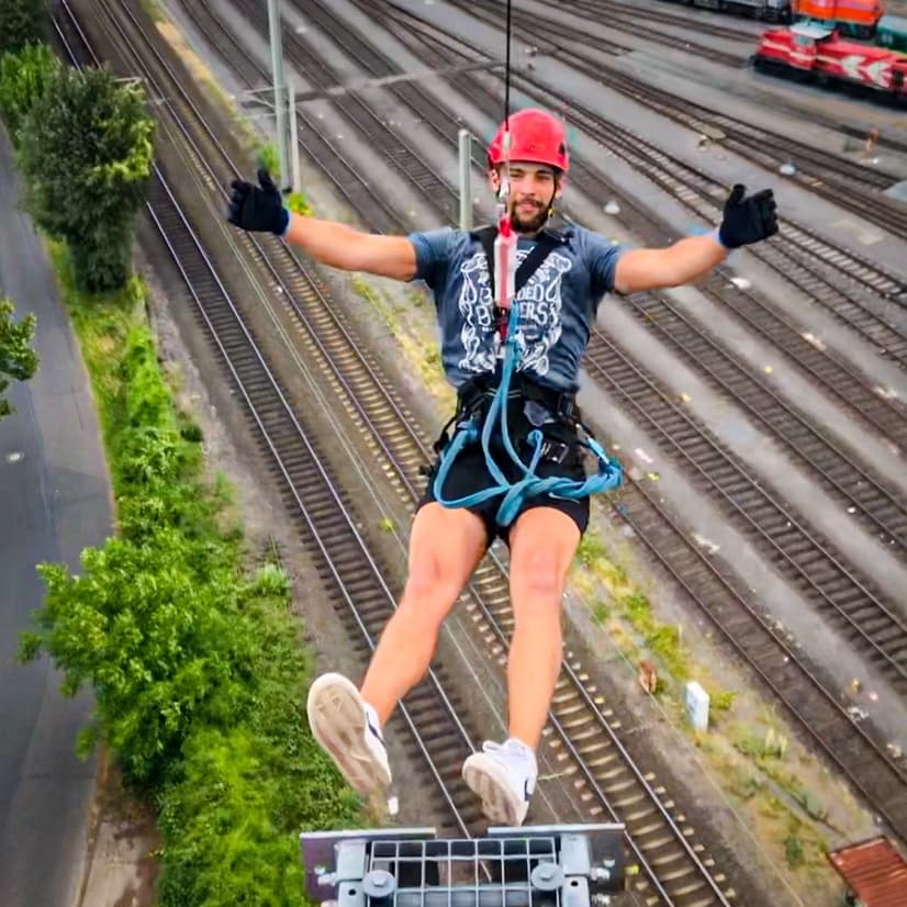 Man ziplining high above railway tracks with urban landscape below