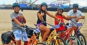 Group of riders cycling on sandy beach with pier backdrop
