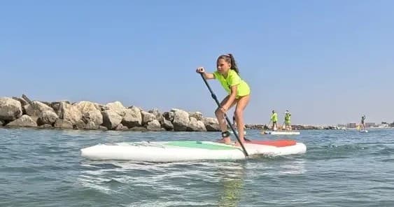 Young paddleboarder near rocky breakwater on sunny Italian coast