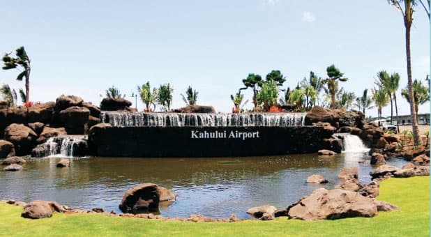 Kahului Airport waterfall sign with palm trees on sunny lawn