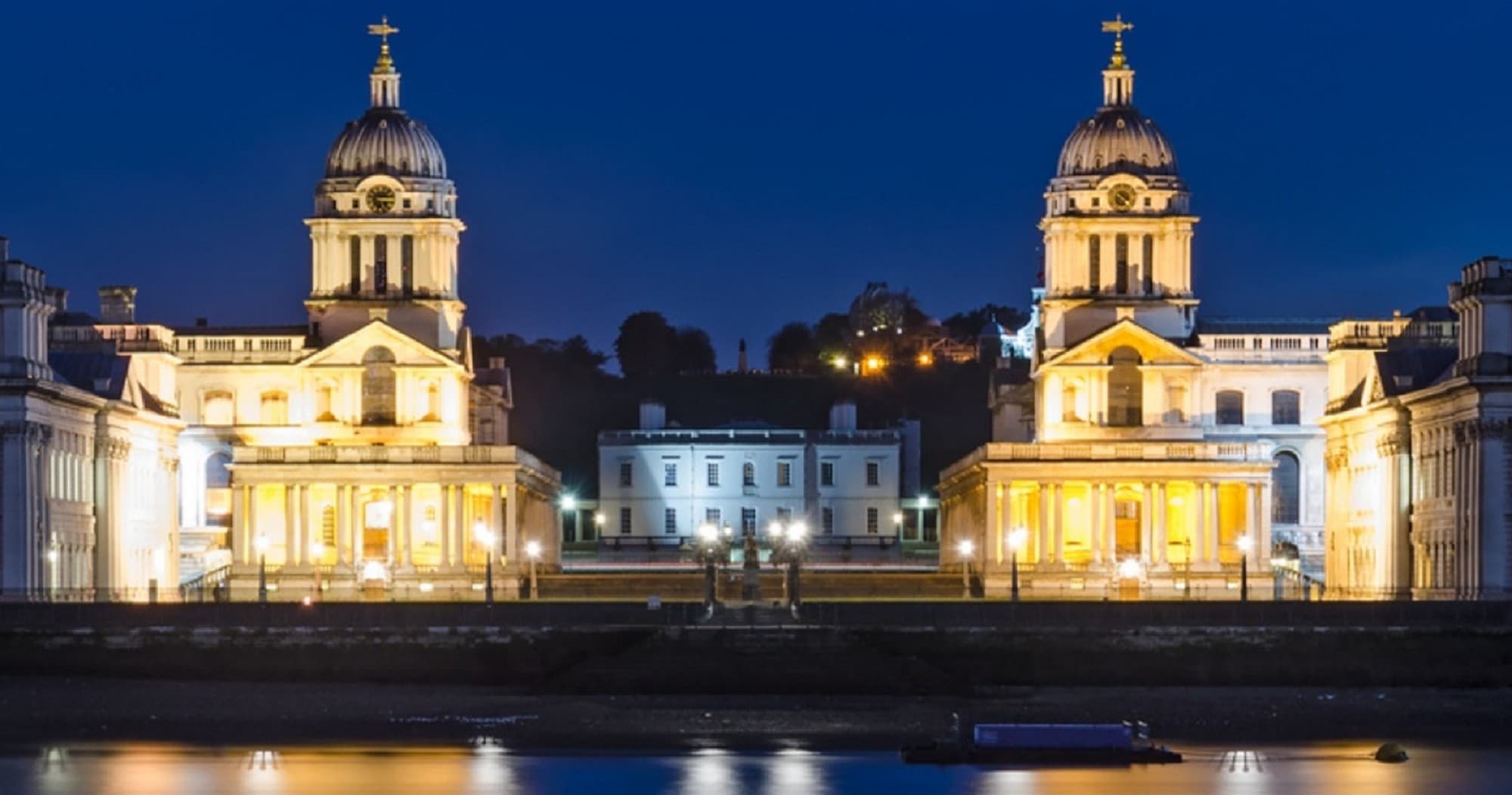 Nighttime riverside view of historic twin churches in Greenwich