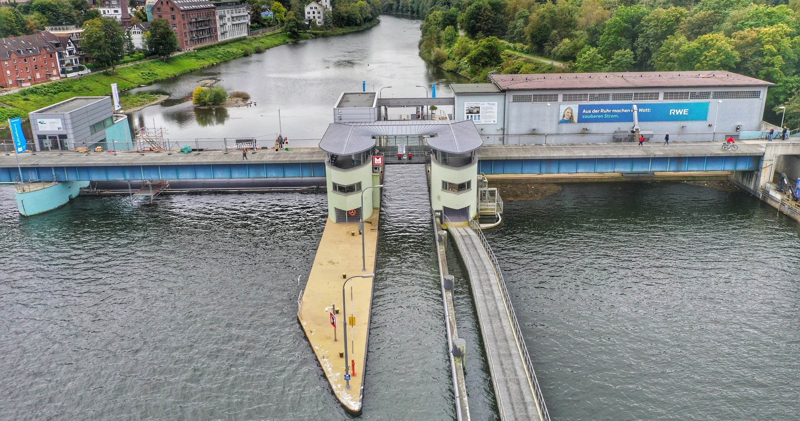 Aerial view of river lock with pedestrian pier and green banks