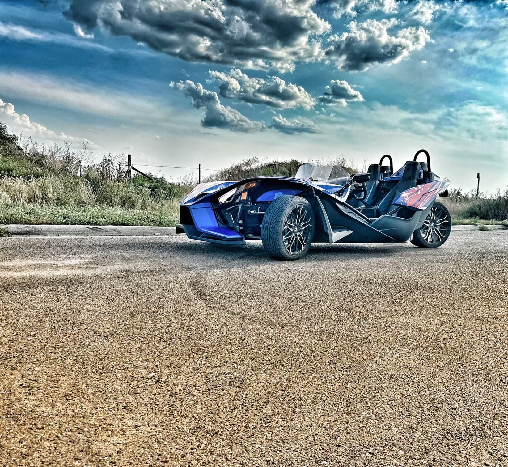 Open-air Slingshot roadster on rural road under dramatic sky