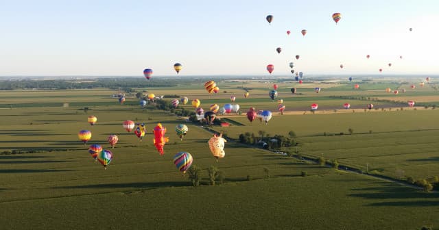 Multiple hot air balloons flying over green farmland at dawn