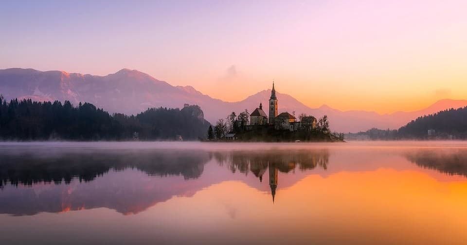 Sunset over island church on tranquil alpine lake with mist