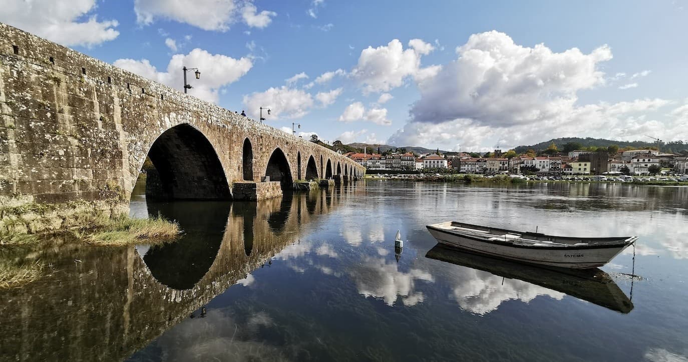 Ancient stone bridge over reflective river with moored boat