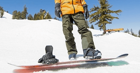 Snowboarder shredding powder on sunlit slope near pine trees