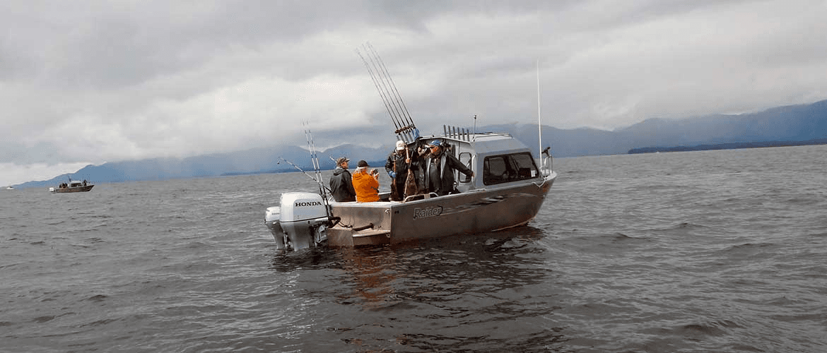 Small fishing charter boat with anglers on open ocean under clouds