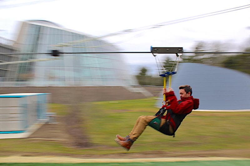 Single rider ziplining past park buildings with motion blur