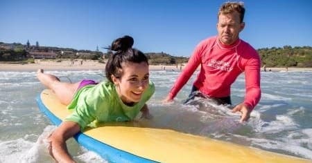Beginner catching wave with instructor guiding on shallow beach