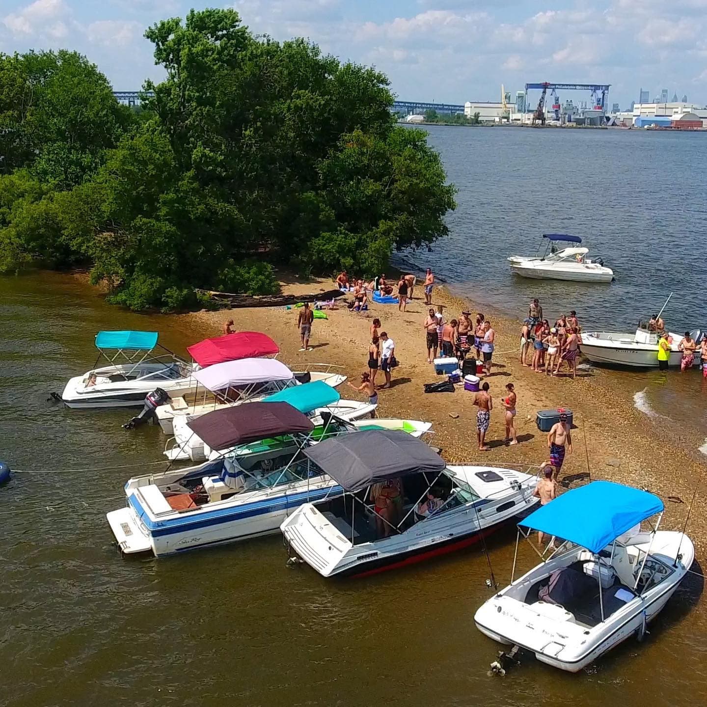 Group anchored at sandy river beach with multiple recreational boats