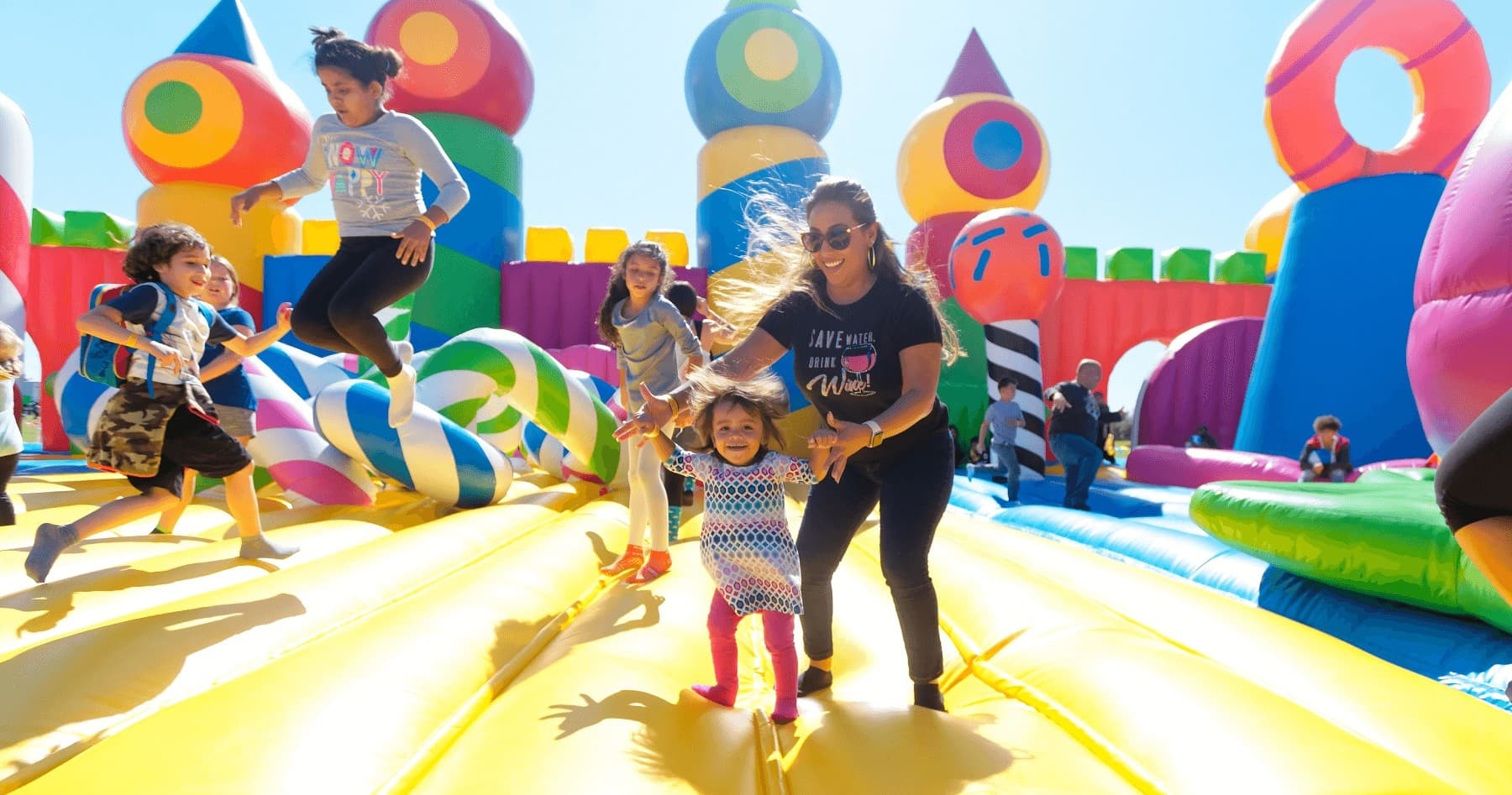 Family running across large outdoor inflatable with bright sunlight
