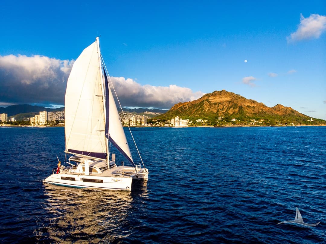 Catamaran sailing off tropical coastline near volcanic headland