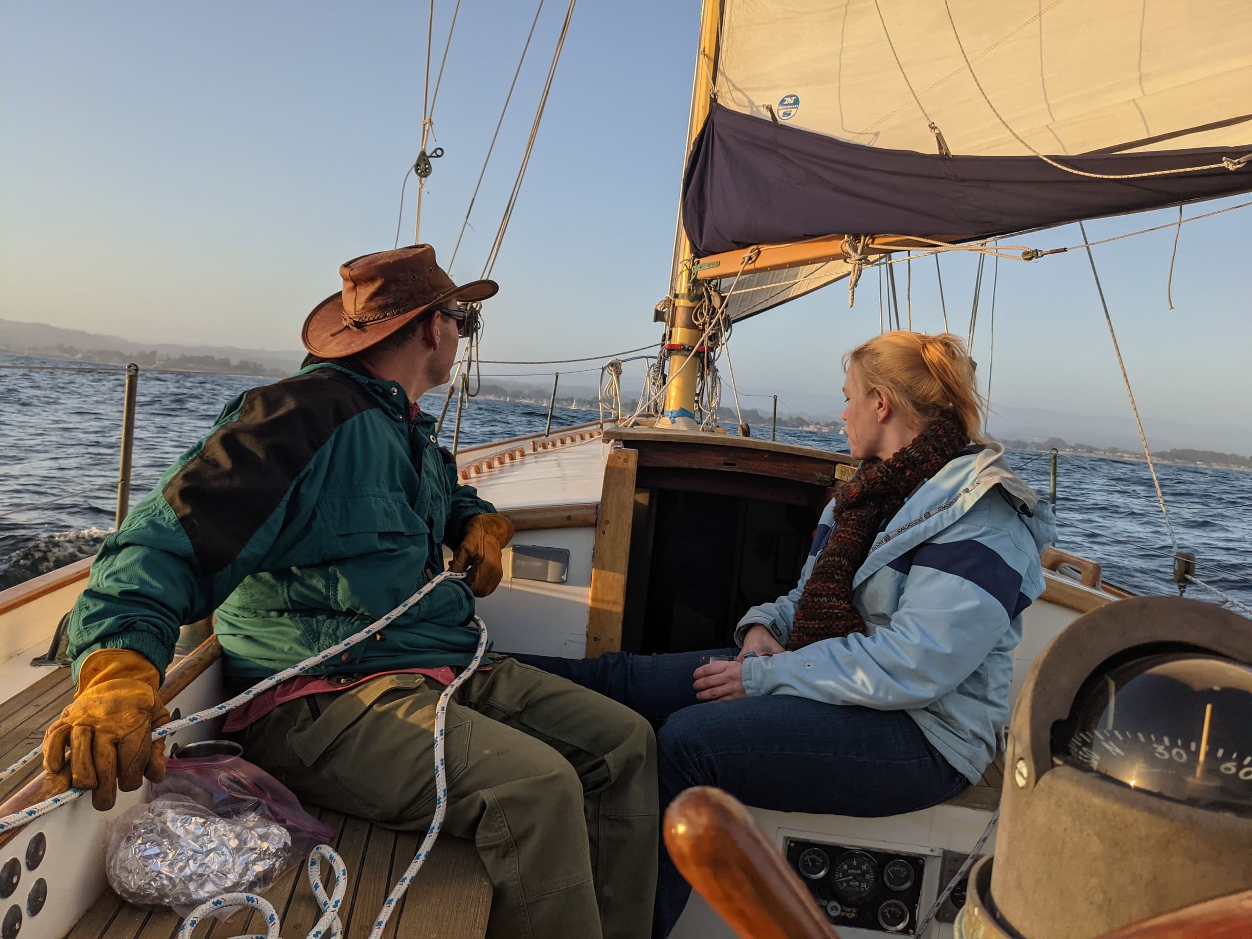 Couple sailing classic sloop off California coast at sunset