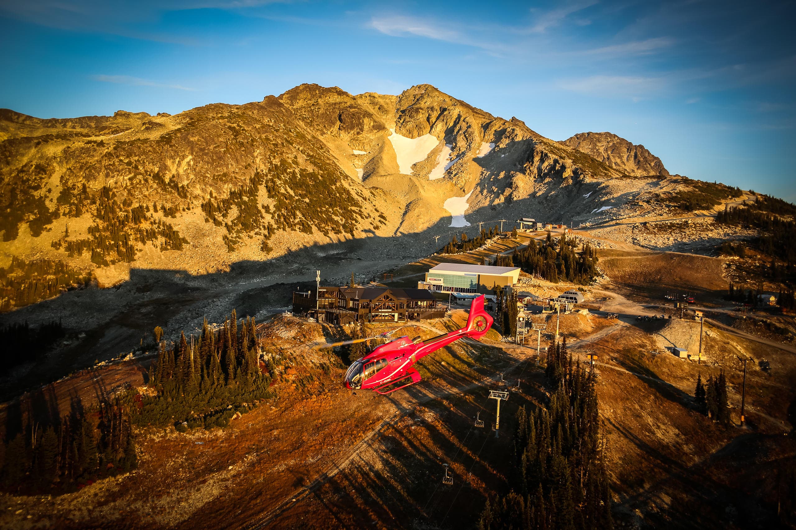 Red helicopter flying over golden alpine ridges at sunset scenery