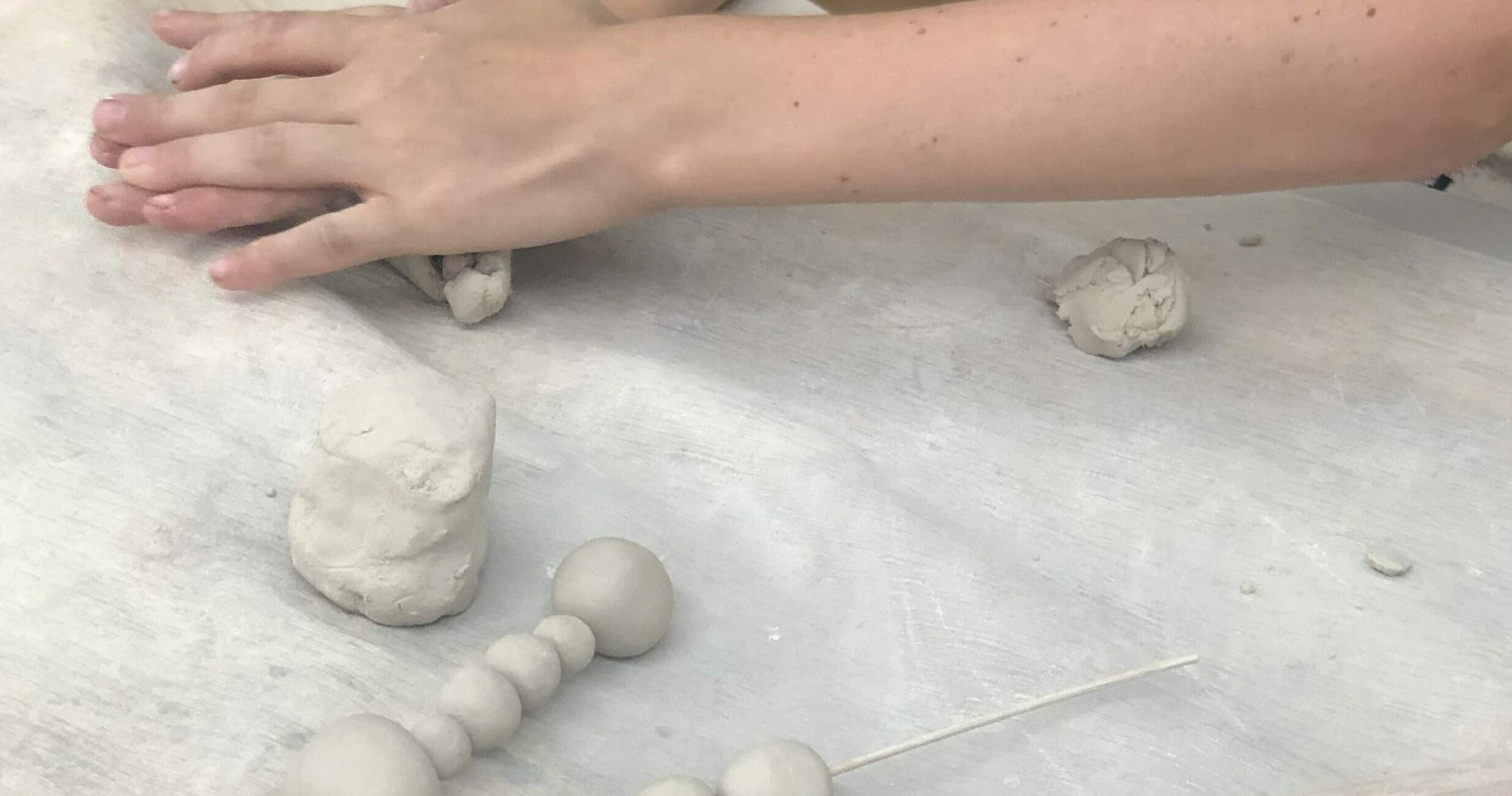 Hands rolling clay beads on workbench during pottery handbuilding session
