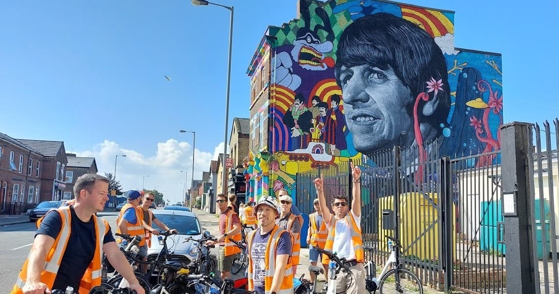 Cycling tour group passing vibrant Beatles mural on city street