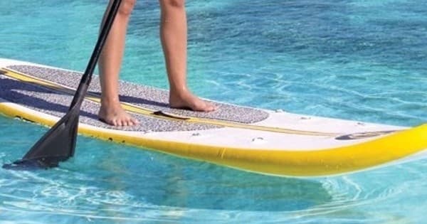 Stand-up paddleboarding on calm tropical water, close-up feet