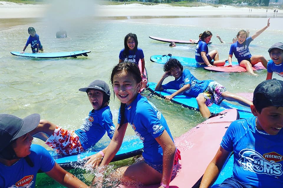 Kids in surf lesson on Broadbeach shore practicing on boards