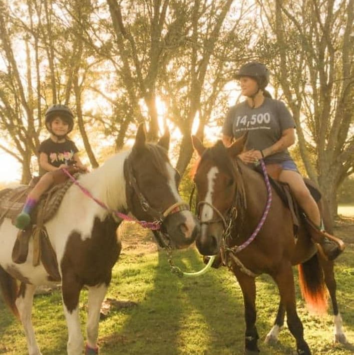 Two children riding horses at sunset under oak trees