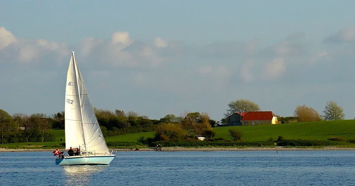 Single sailboat cruising calm river waters near green shoreline