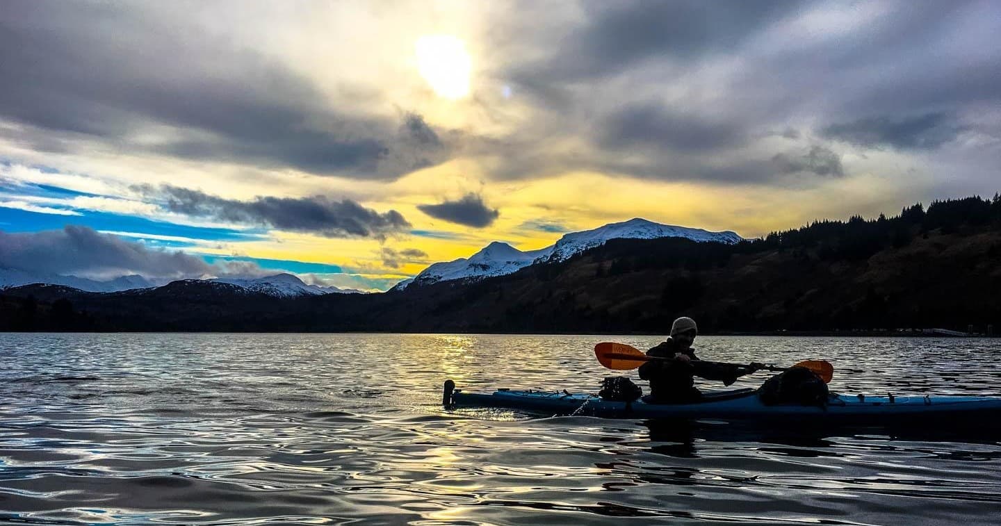 Silhouette kayaker paddling at sunset with dramatic mountain sky