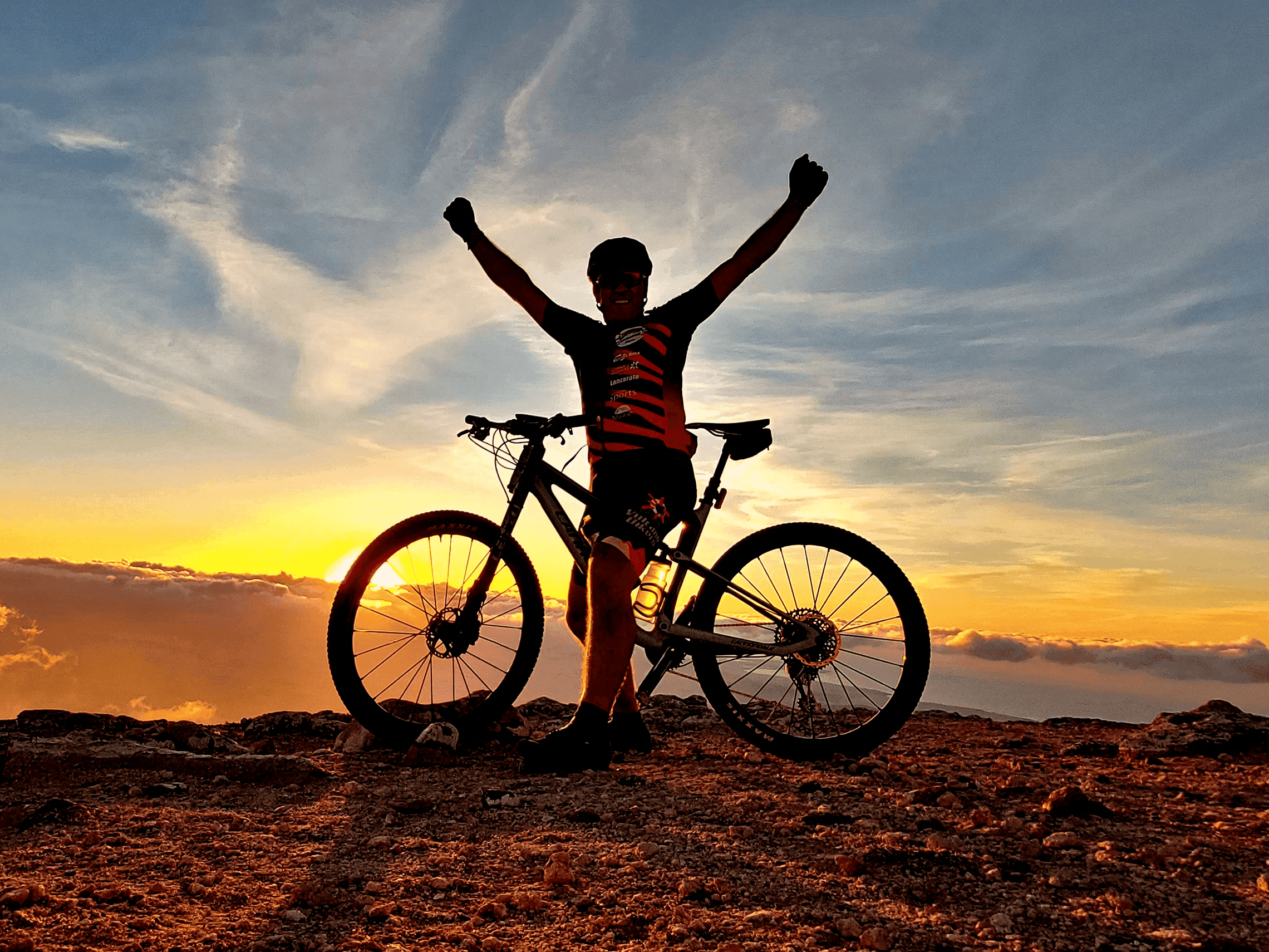 Cyclist silhouetted at sunset on volcanic coastal trail