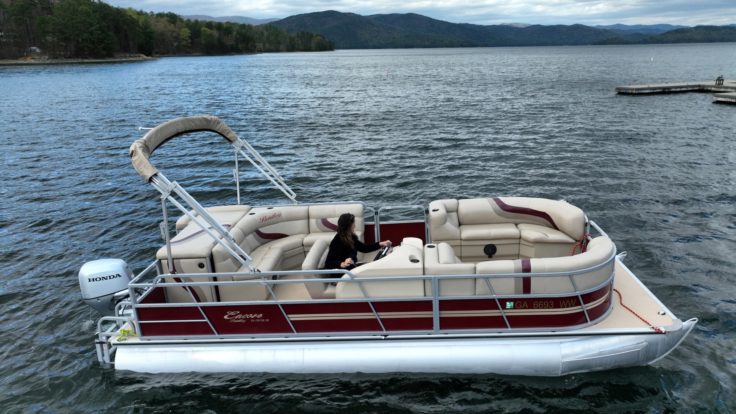 Red pontoon boat cruising calm lake with tree-lined shore