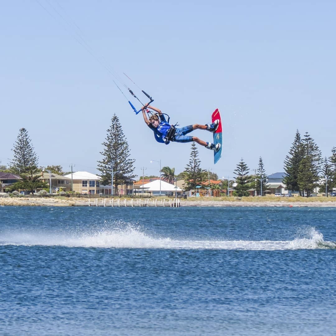 Kiteboarder airborne over choppy coastal water with shoreline trees