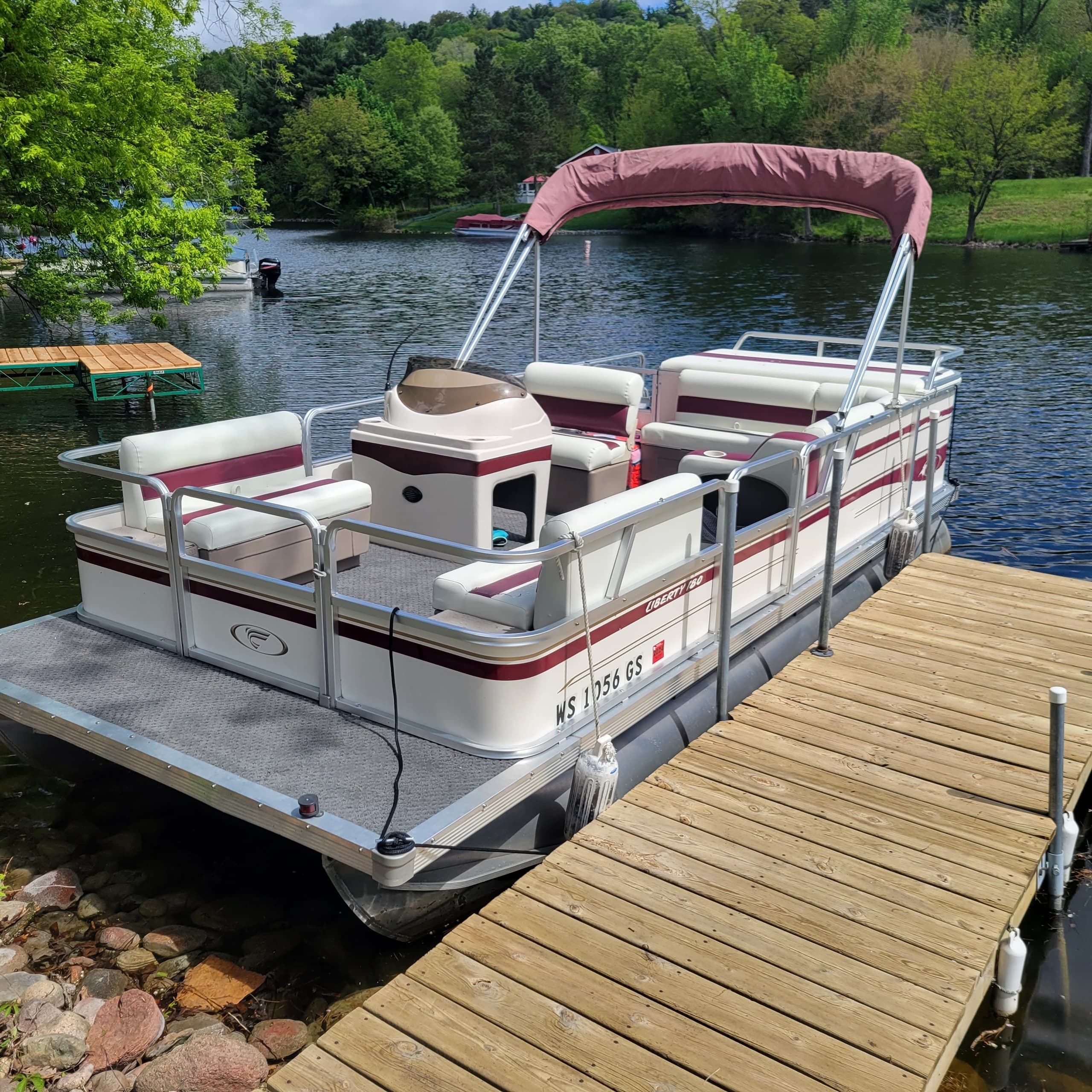 Pontoon boat docked on wooded lake shore, calm summer scene