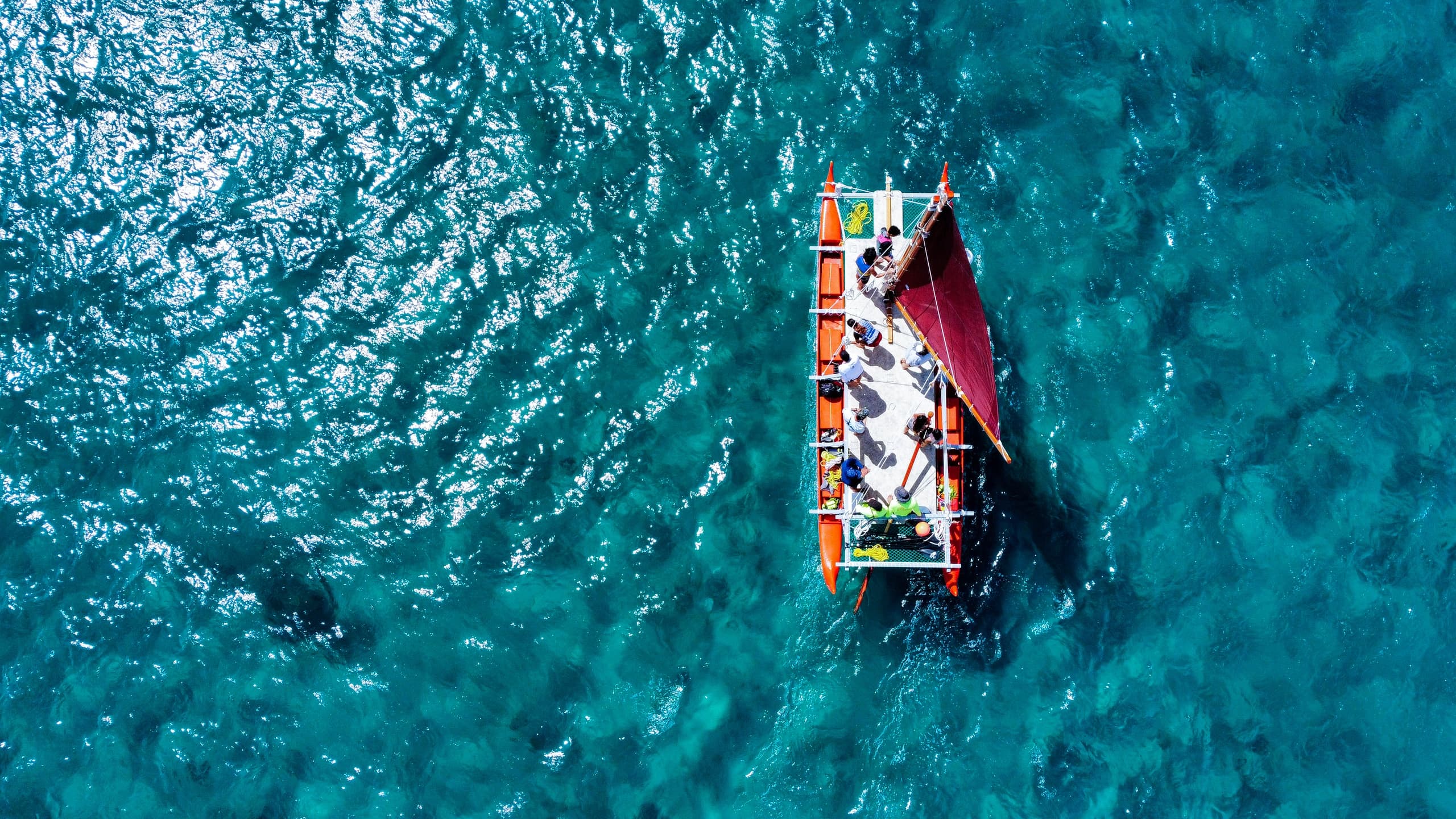 Aerial view of outrigger canoe on clear turquoise ocean waters