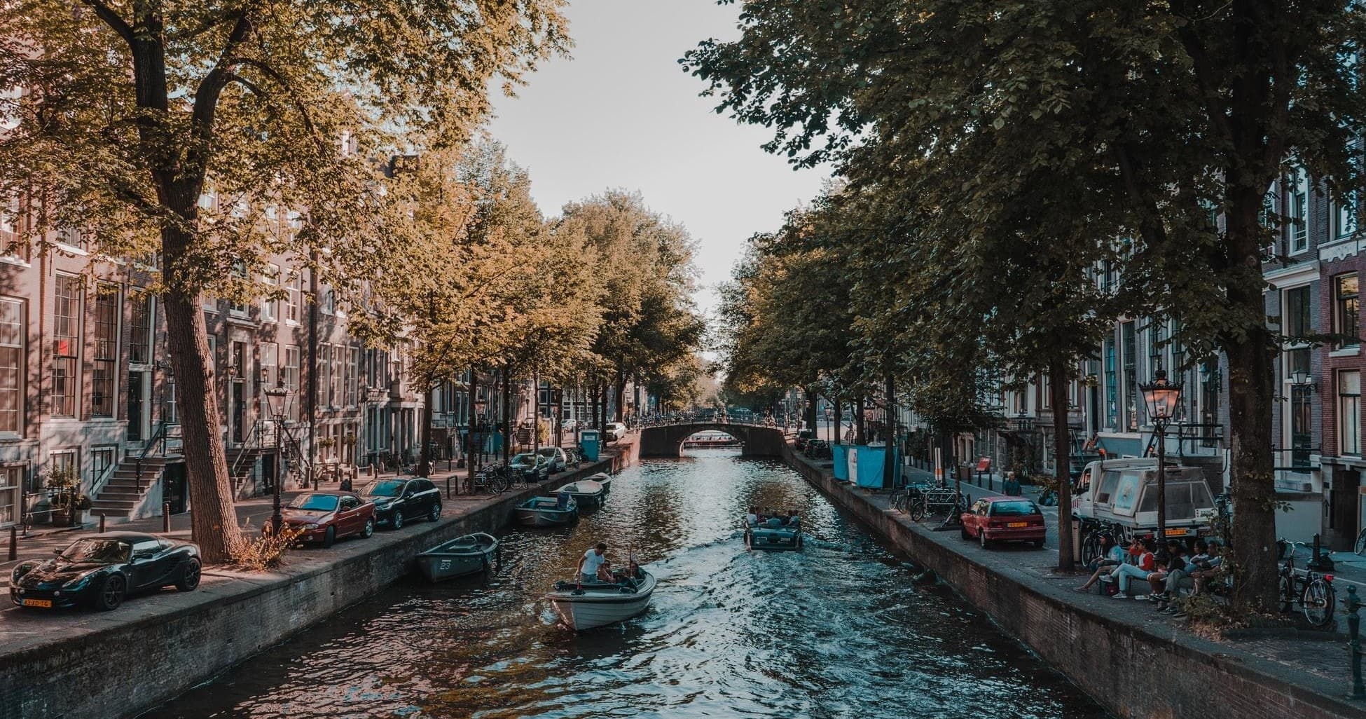 Small boat navigating narrow Amsterdam canal under leafy trees