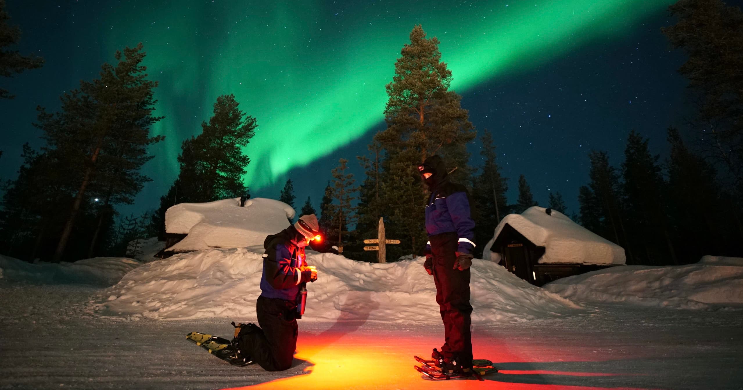 People viewing northern lights over snowy campsite with aurora